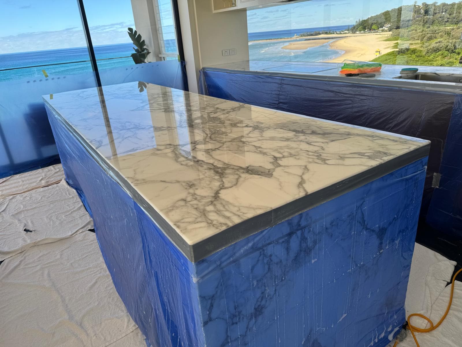 Calacatta marble kitchen island polished on site, cabinetry masked in protective blue film